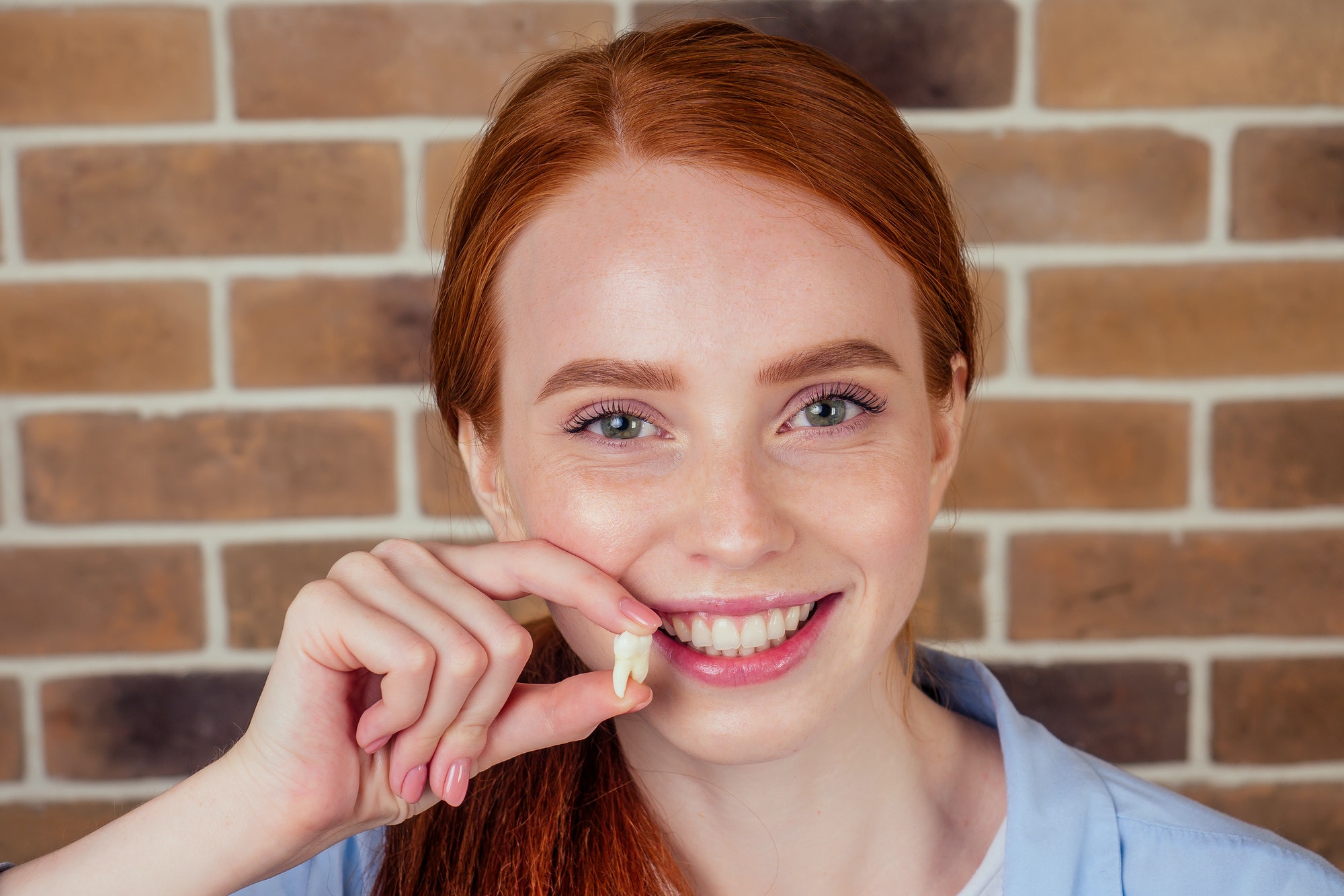 redhaired ginger female with snow-white smile holding white wisdom tooth after surgery