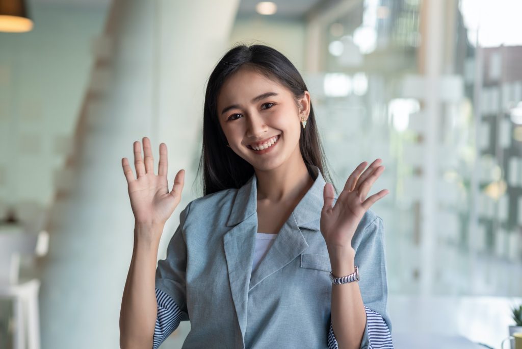 Asian businesswoman raises your hand while smiling. Looking at camera.