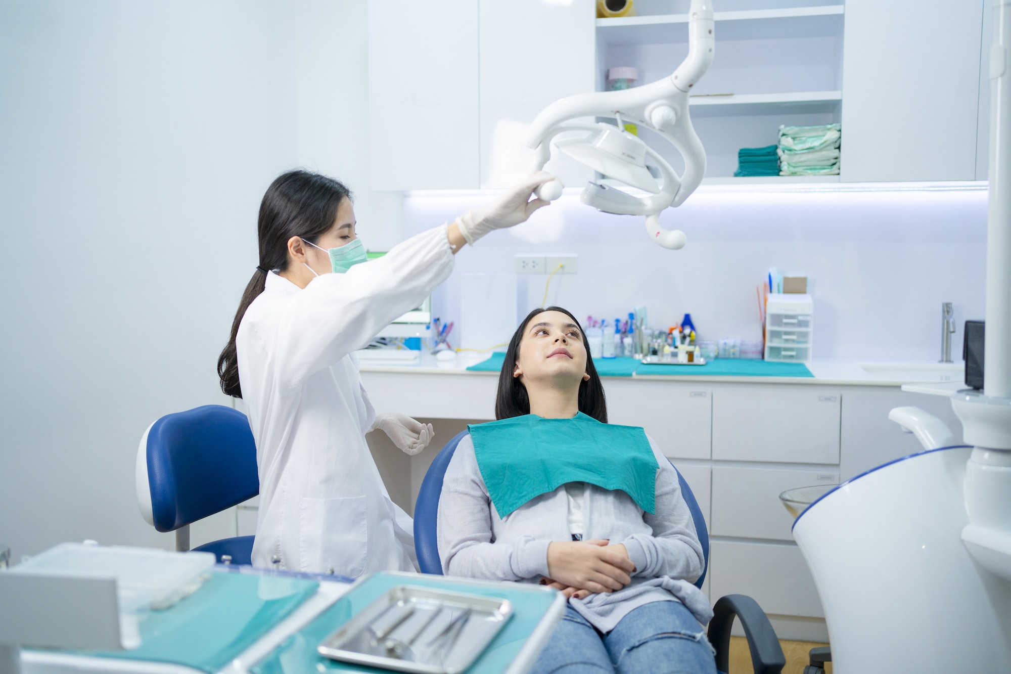 Asian female dentist adjust dental surgical light then start checking or examining tooth of patient