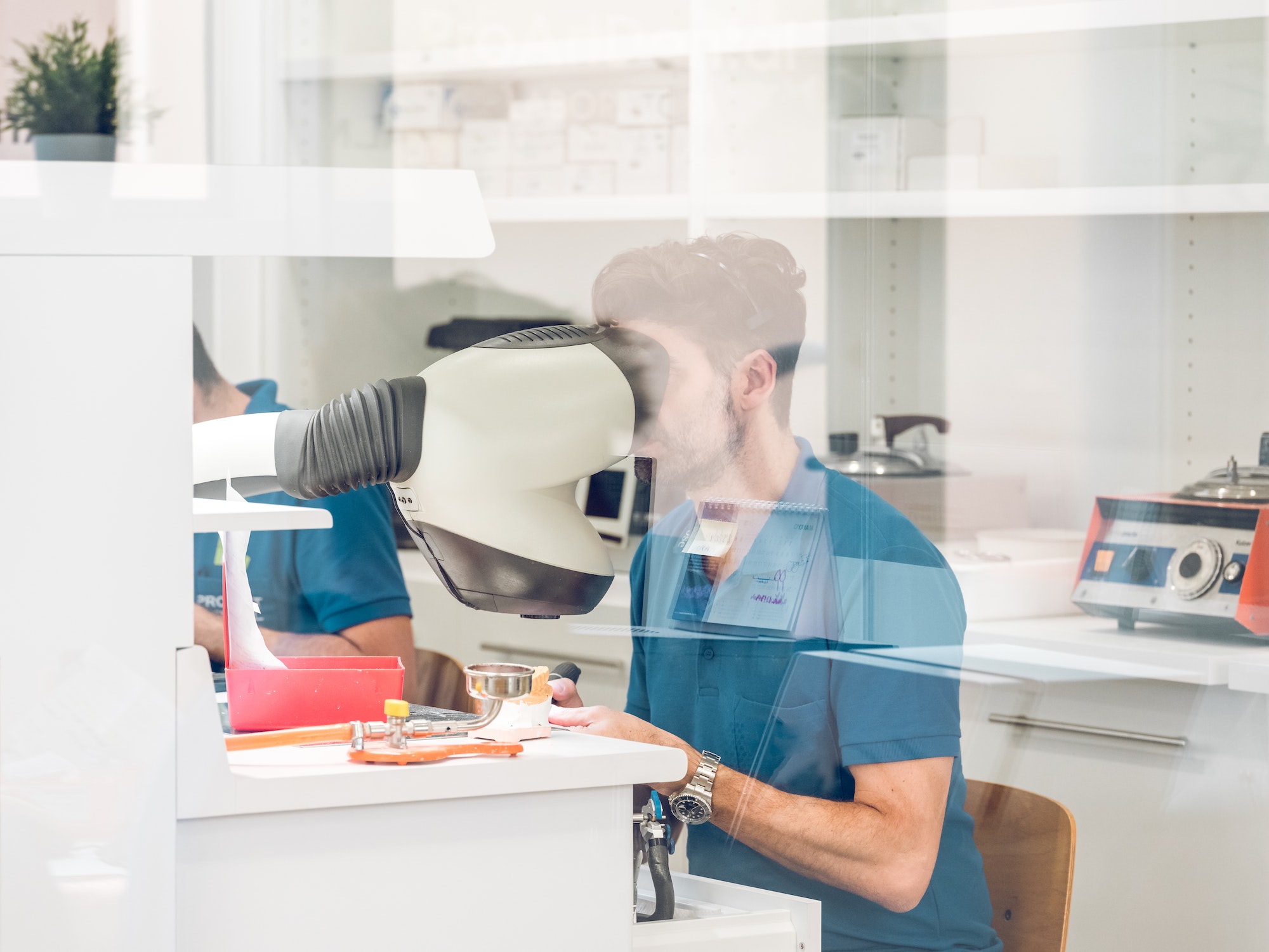 Dental technician man preparing jaw denture in microscope in laboratory