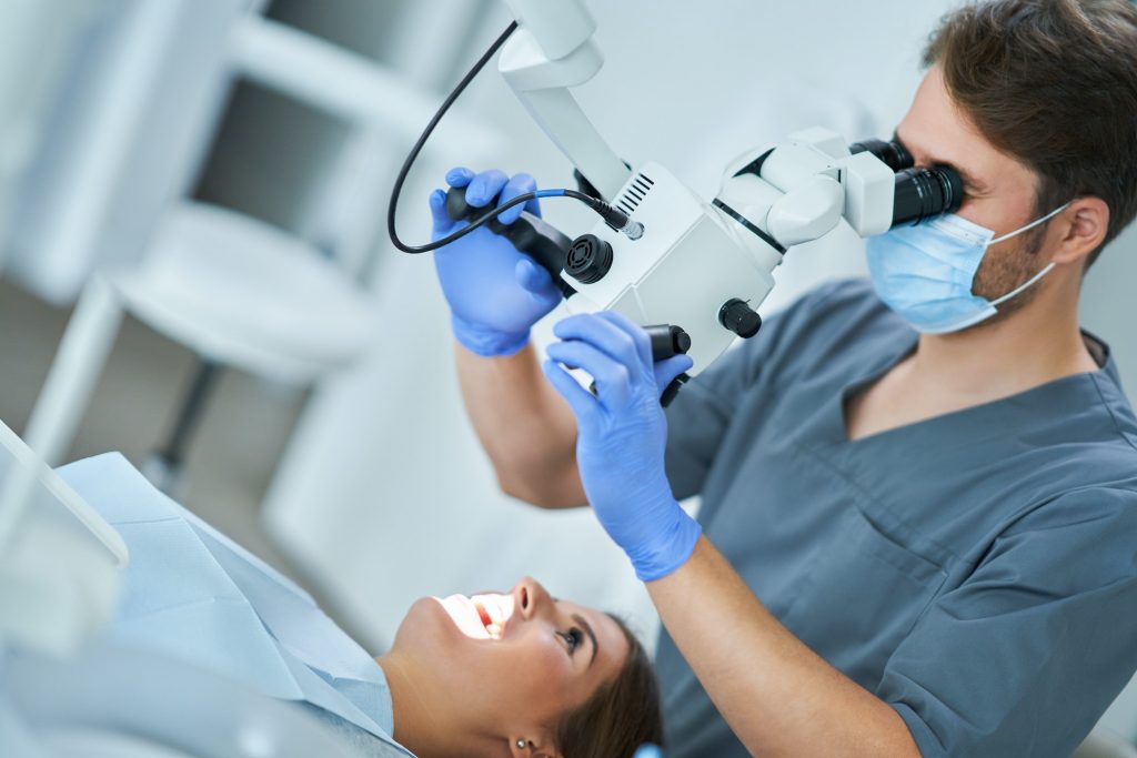 Dentist checking up patient teeth with microscope at surgery office