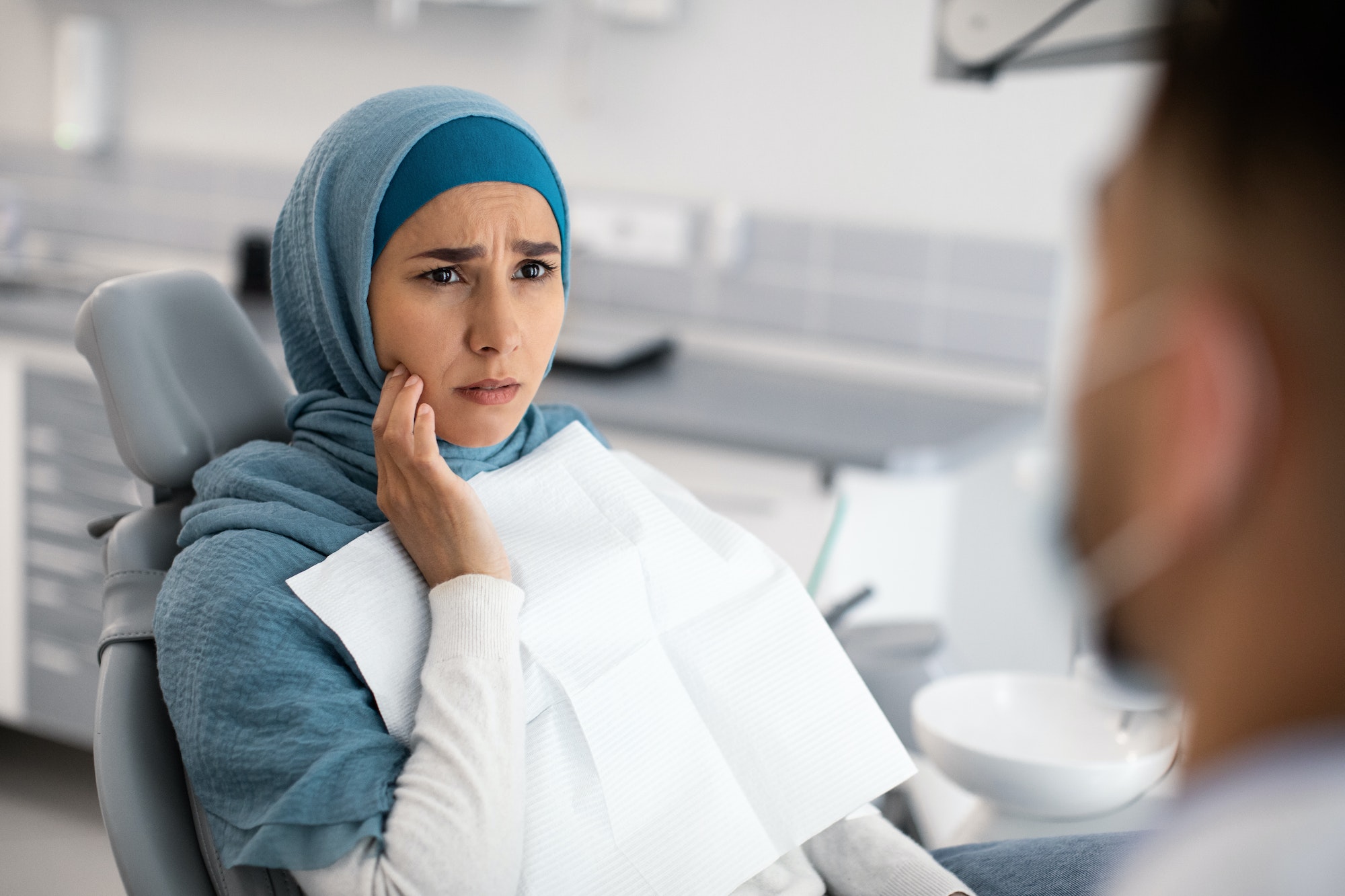 Teeth Problems. Muslim Female In Dentist Chair Showing Aching Tooth To Doctor