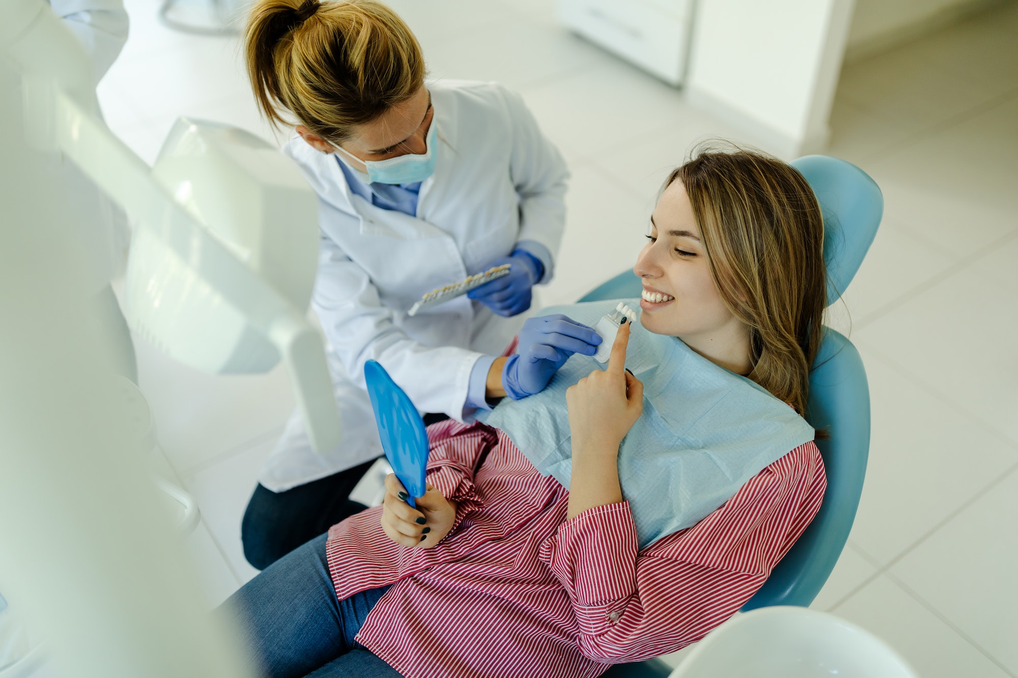 Young woman sitting in dental chair and selecting best color of implants using teeth samples.